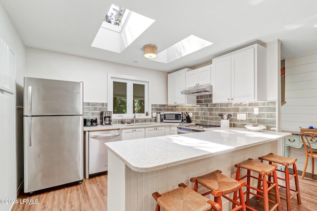 kitchen with sink, a breakfast bar, appliances with stainless steel finishes, backsplash, and white cabinets