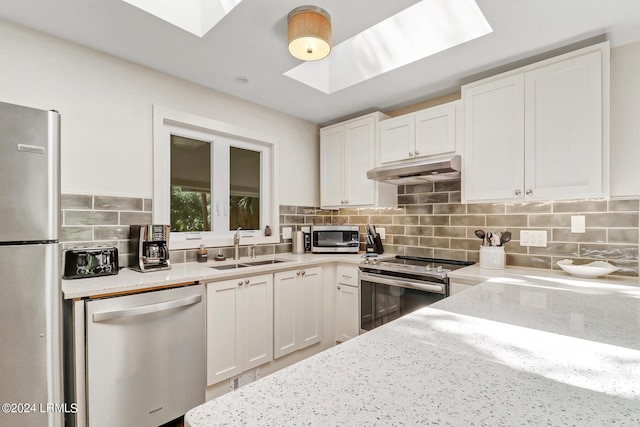 kitchen featuring sink, a skylight, stainless steel appliances, tasteful backsplash, and white cabinets