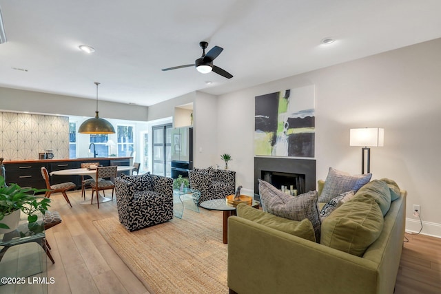 living room featuring ceiling fan, sink, and light wood-type flooring