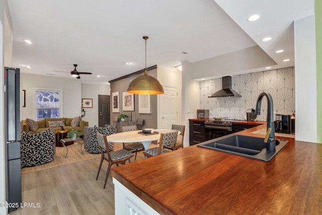 kitchen featuring stainless steel electric stove, sink, black fridge, light wood-type flooring, and wall chimney exhaust hood