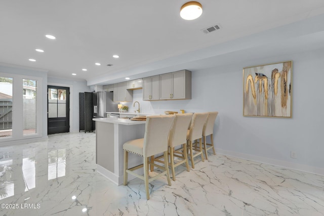 kitchen featuring baseboards, visible vents, stainless steel fridge with ice dispenser, light countertops, and a kitchen bar