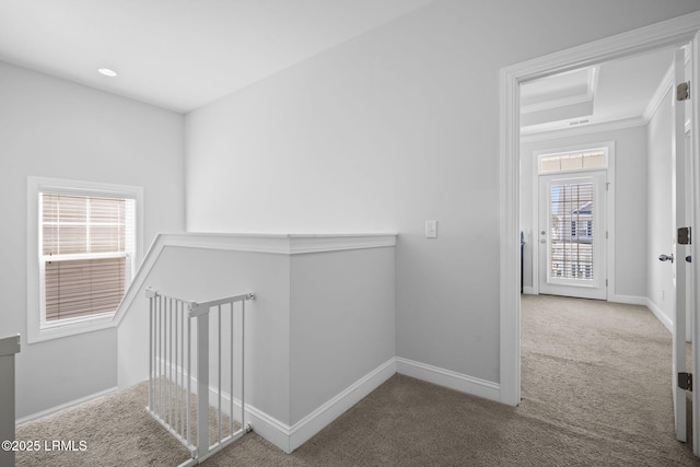 corridor featuring carpet, a raised ceiling, ornamental molding, an upstairs landing, and baseboards