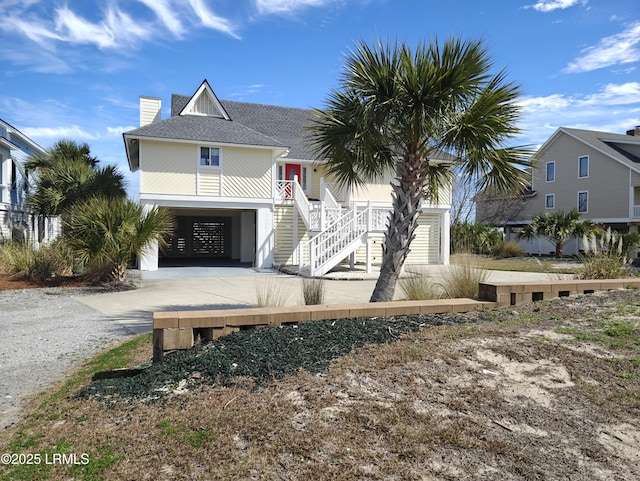 beach home with a chimney, a shingled roof, stairway, a carport, and driveway