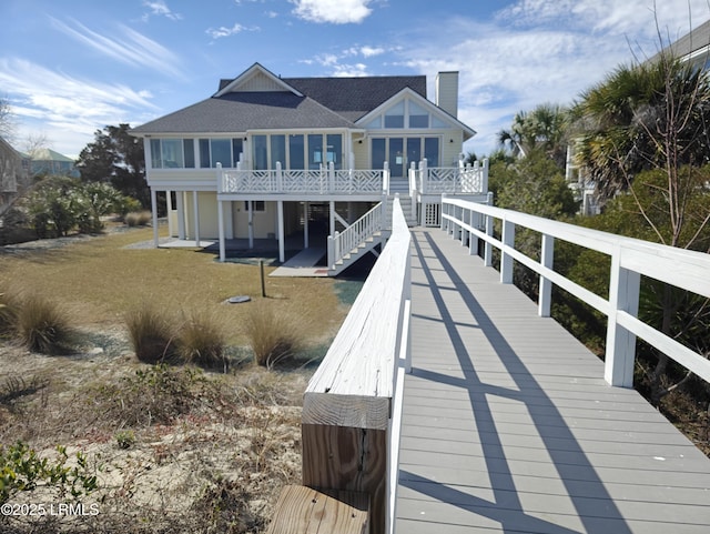 rear view of property with a shingled roof, a lawn, a chimney, and stairs