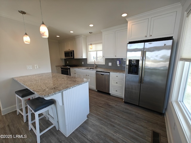 kitchen with appliances with stainless steel finishes, a sink, white cabinetry, and decorative light fixtures