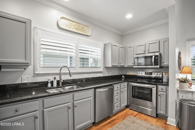 kitchen featuring dark stone counters, appliances with stainless steel finishes, ornamental molding, gray cabinets, and a sink