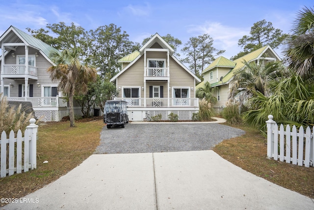 view of front facade featuring gravel driveway, covered porch, a balcony, and fence