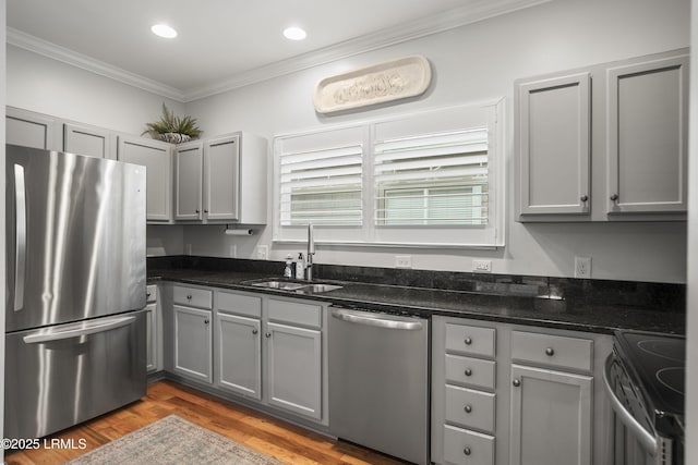 kitchen with appliances with stainless steel finishes, ornamental molding, dark stone countertops, gray cabinetry, and a sink