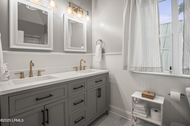 bathroom featuring a wainscoted wall, double vanity, and a sink