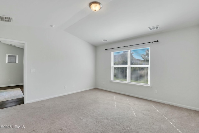 carpeted spare room featuring vaulted ceiling, visible vents, and baseboards