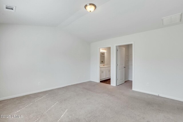 unfurnished bedroom with ensuite bathroom, carpet floors, visible vents, baseboards, and a spacious closet