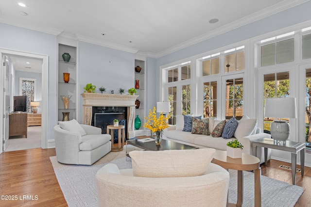 living room with built in shelves, a high end fireplace, ornamental molding, and light wood-type flooring