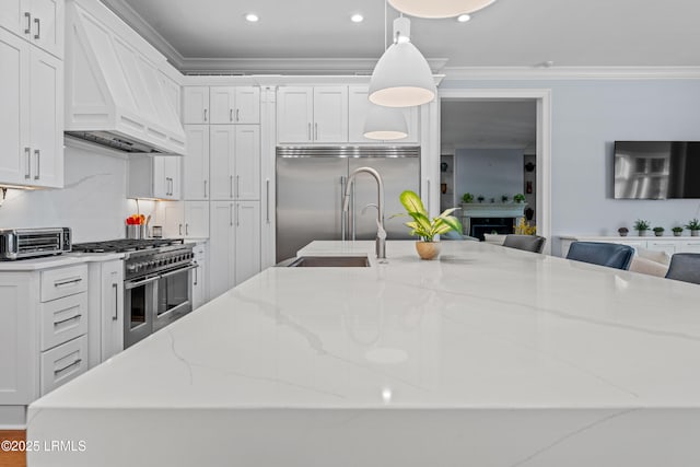 kitchen with high end appliances, light stone counters, hanging light fixtures, custom range hood, and white cabinets