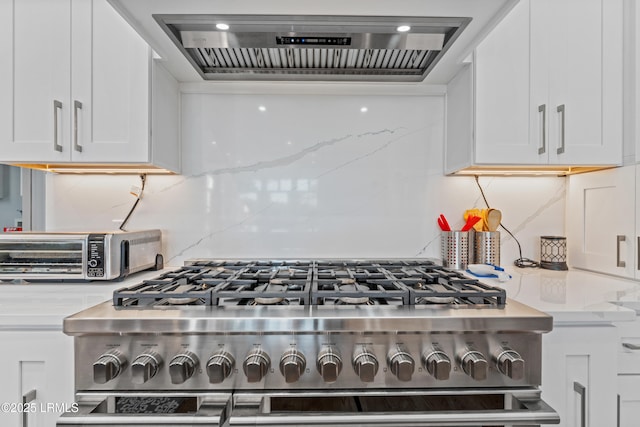 kitchen with high end range, light stone counters, white cabinets, decorative backsplash, and wall chimney exhaust hood