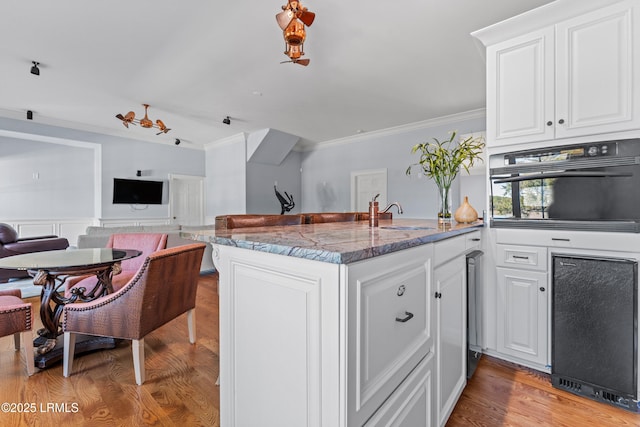 kitchen with stone counters, white cabinetry, oven, ornamental molding, and light wood-type flooring