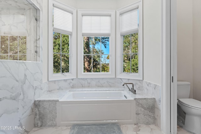 bathroom with a tub to relax in and toilet