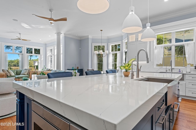 kitchen with pendant lighting, a kitchen island with sink, light stone counters, and a wealth of natural light