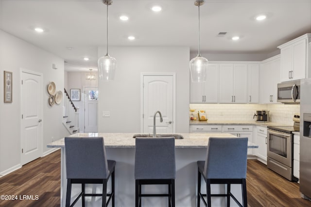 kitchen with appliances with stainless steel finishes, decorative light fixtures, white cabinetry, sink, and a kitchen island with sink