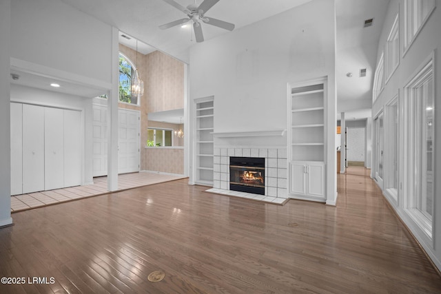 647 Island Cir E, Saint Helena Island, SC 29920 - unfurnished living room featuring a towering ceiling, wood finished floors, a tiled fireplace, built in features, and ceiling fan