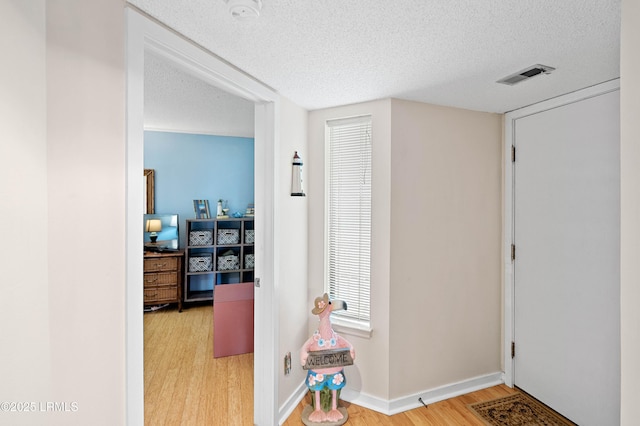 entryway featuring a textured ceiling, wood finished floors, visible vents, and baseboards