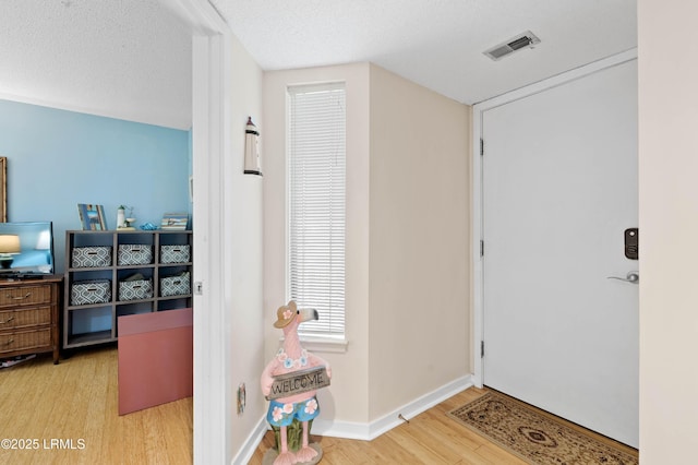 interior space with visible vents, a textured ceiling, baseboards, and wood finished floors