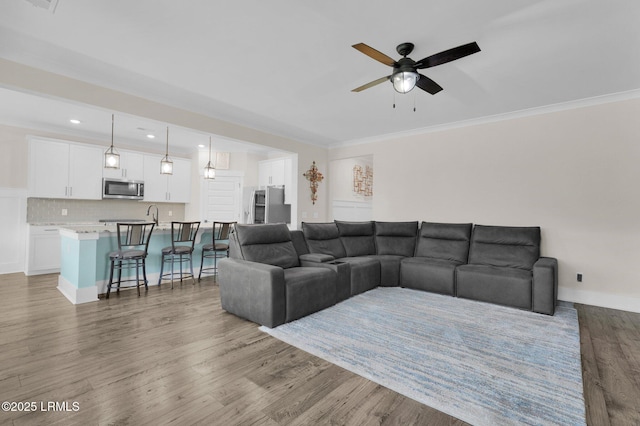 living area featuring crown molding, baseboards, recessed lighting, wood finished floors, and a ceiling fan