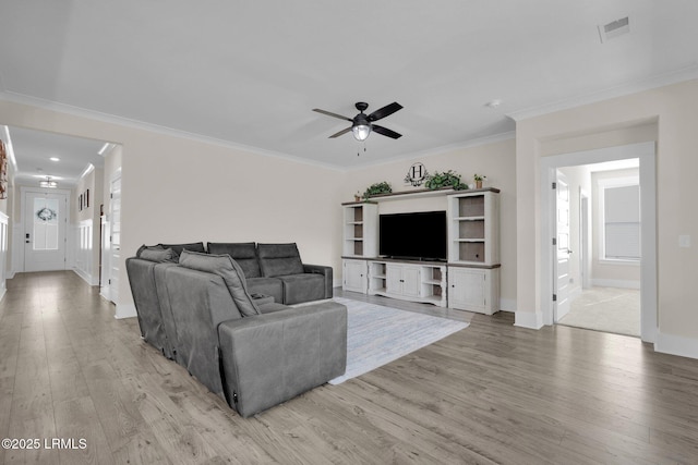 living room with light wood-type flooring, a ceiling fan, visible vents, baseboards, and ornamental molding