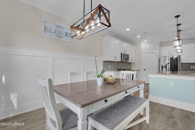 dining room with recessed lighting, light wood-style flooring, a chandelier, ornamental molding, and a wainscoted wall