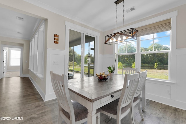 dining area with wood finished floors, a decorative wall, wainscoting, visible vents, and a notable chandelier