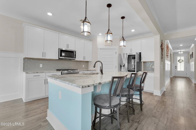 kitchen with appliances with stainless steel finishes, ornamental molding, light wood finished floors, a sink, and a kitchen breakfast bar