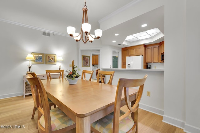 dining area with ornamental molding, an inviting chandelier, light hardwood / wood-style floors, and a skylight