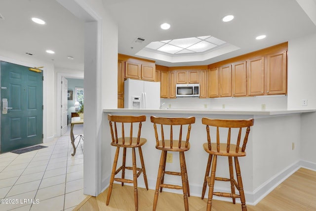 kitchen featuring a skylight, light brown cabinetry, white refrigerator with ice dispenser, and a breakfast bar area