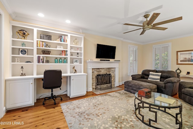 living area with ornamental molding, built in desk, a fireplace, and light wood-style floors