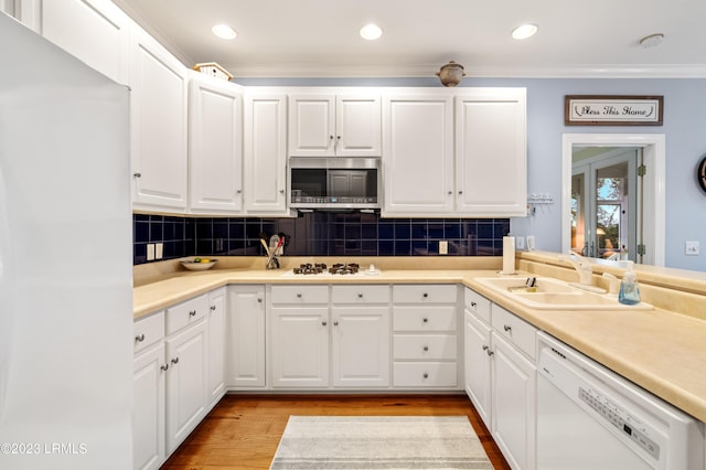 kitchen with white appliances, a sink, white cabinets, ornamental molding, and light wood finished floors