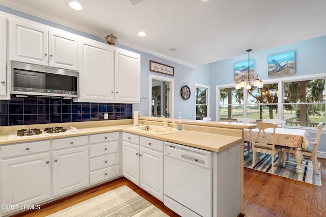 kitchen featuring light wood-style flooring, a peninsula, white appliances, a sink, and decorative backsplash