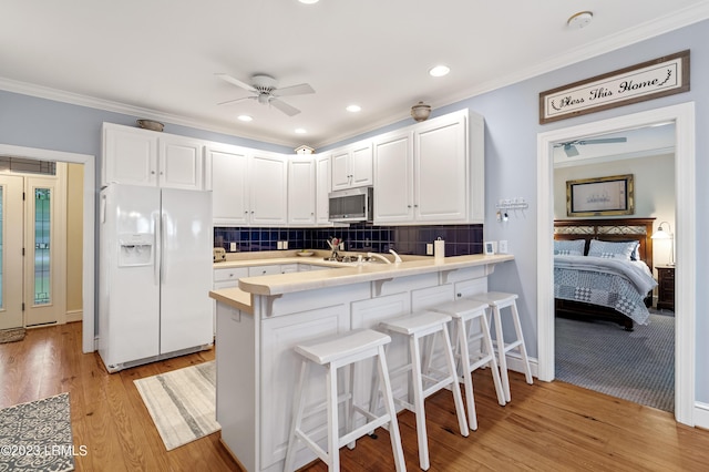 kitchen featuring a peninsula, light wood-type flooring, white fridge with ice dispenser, stainless steel microwave, and crown molding