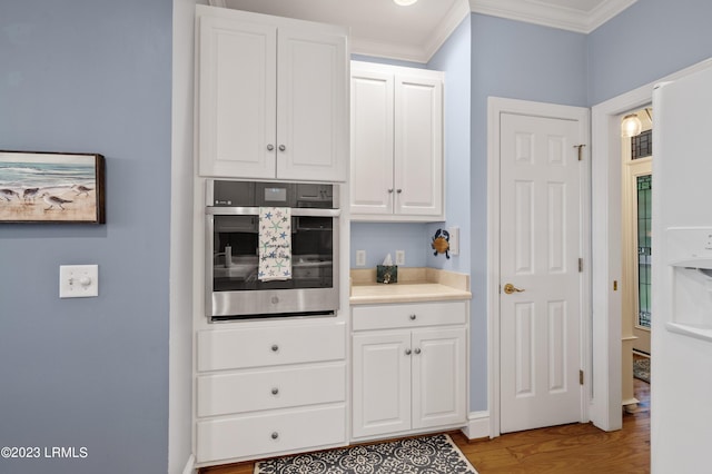 kitchen featuring wood finished floors, oven, light countertops, crown molding, and white cabinetry