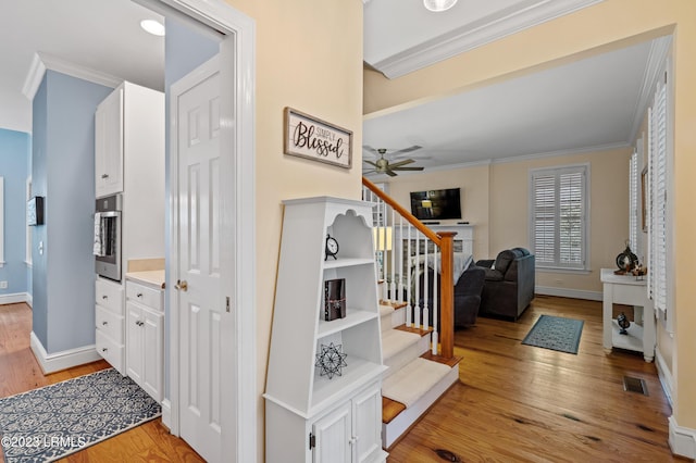 stairs with visible vents, baseboards, a ceiling fan, wood finished floors, and crown molding