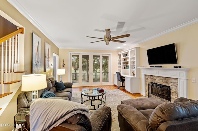 living room featuring ceiling fan, ornamental molding, a fireplace, and light wood-style flooring