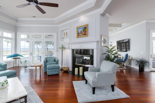 living room featuring built in shelves, dark hardwood / wood-style floors, a tile fireplace, and crown molding