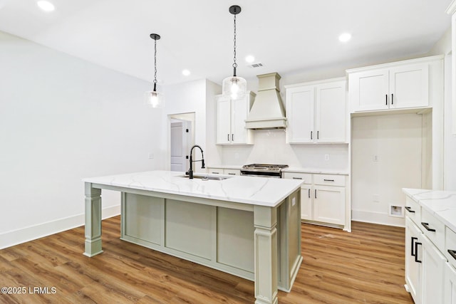 kitchen with premium range hood, sink, white cabinetry, an island with sink, and pendant lighting