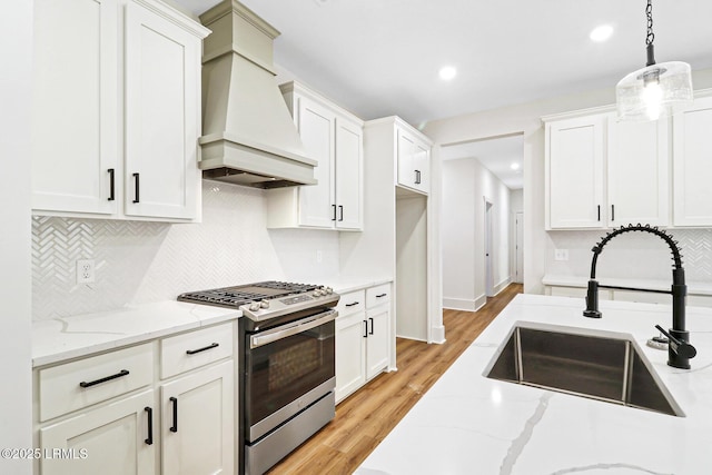 kitchen featuring sink, white cabinetry, hanging light fixtures, stainless steel range with gas cooktop, and custom range hood