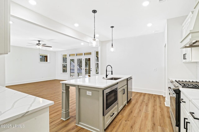 kitchen with sink, decorative light fixtures, an island with sink, stainless steel appliances, and white cabinets