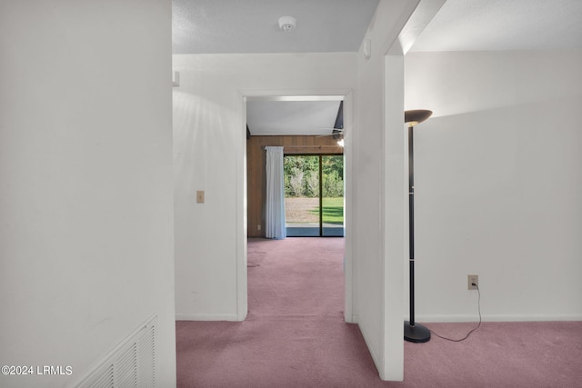 corridor featuring lofted ceiling, light colored carpet, and wood walls