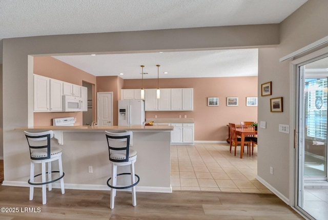 kitchen with a peninsula, white appliances, white cabinets, light countertops, and a kitchen bar