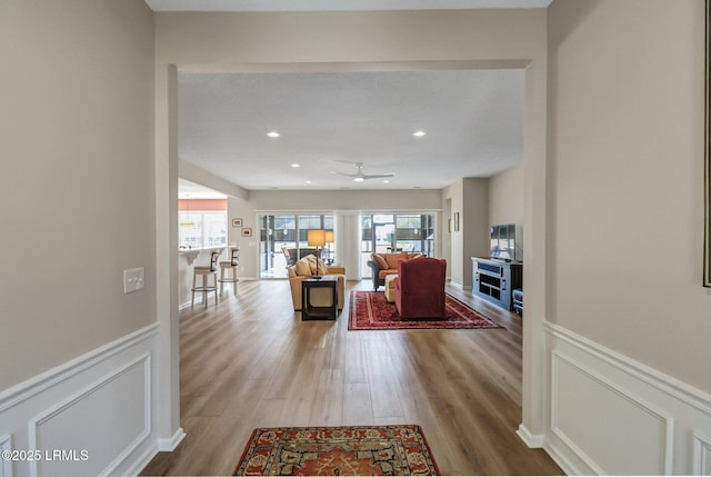 interior space featuring wainscoting, wood finished floors, a ceiling fan, and a decorative wall