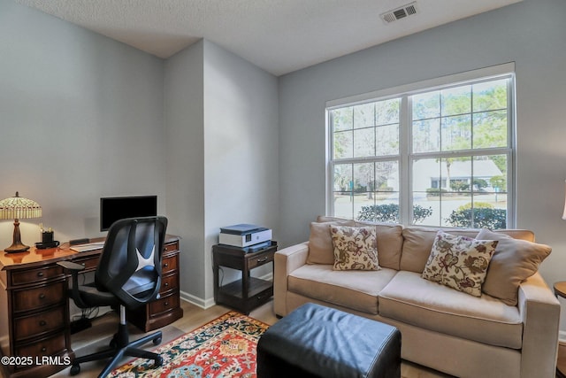 office space with visible vents, light wood finished floors, baseboards, and a textured ceiling