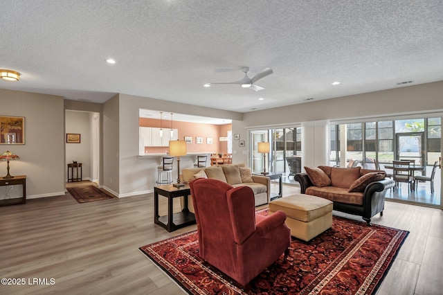 living area featuring baseboards, visible vents, a textured ceiling, and light wood finished floors