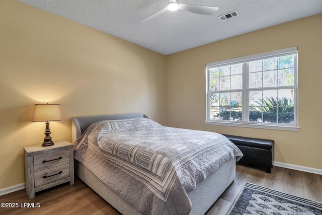 bedroom with baseboards, a textured ceiling, visible vents, and wood finished floors