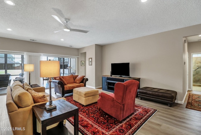 living room with ceiling fan, a textured ceiling, wood finished floors, and baseboards